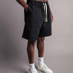 Schräge Perspektive vom Model das die schwarzen TELLEM Baumwoll Shorts aus Cotton Twill mit lockerem Fit trägt und Hand in Hosentasche hat.