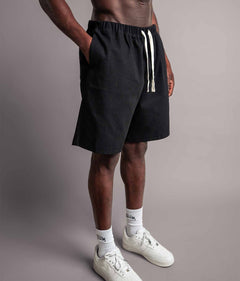 Schräge Perspektive vom Model das die schwarzen TELLEM Baumwoll Shorts aus Cotton Twill mit lockerem Fit trägt und Hand in Hosentasche hat.