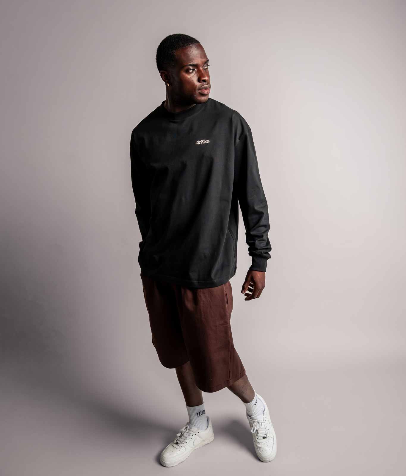Model trägt das schwarze TELLEM Longsleeve aus 100 % Baumwolle mit lockerem Fit zu kurzer Hose