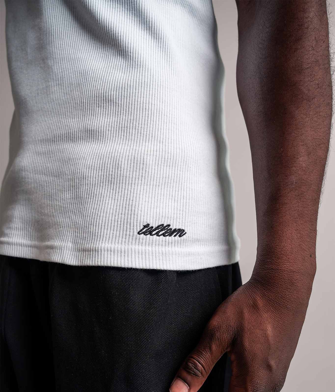 Detailaufnahme des gestickten TELLEM Signature Logos am Saum des weißen Tanktops. LEO